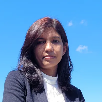 Taslima looks slightly down towards the camera with a neutral face. The clear blue sky behind her