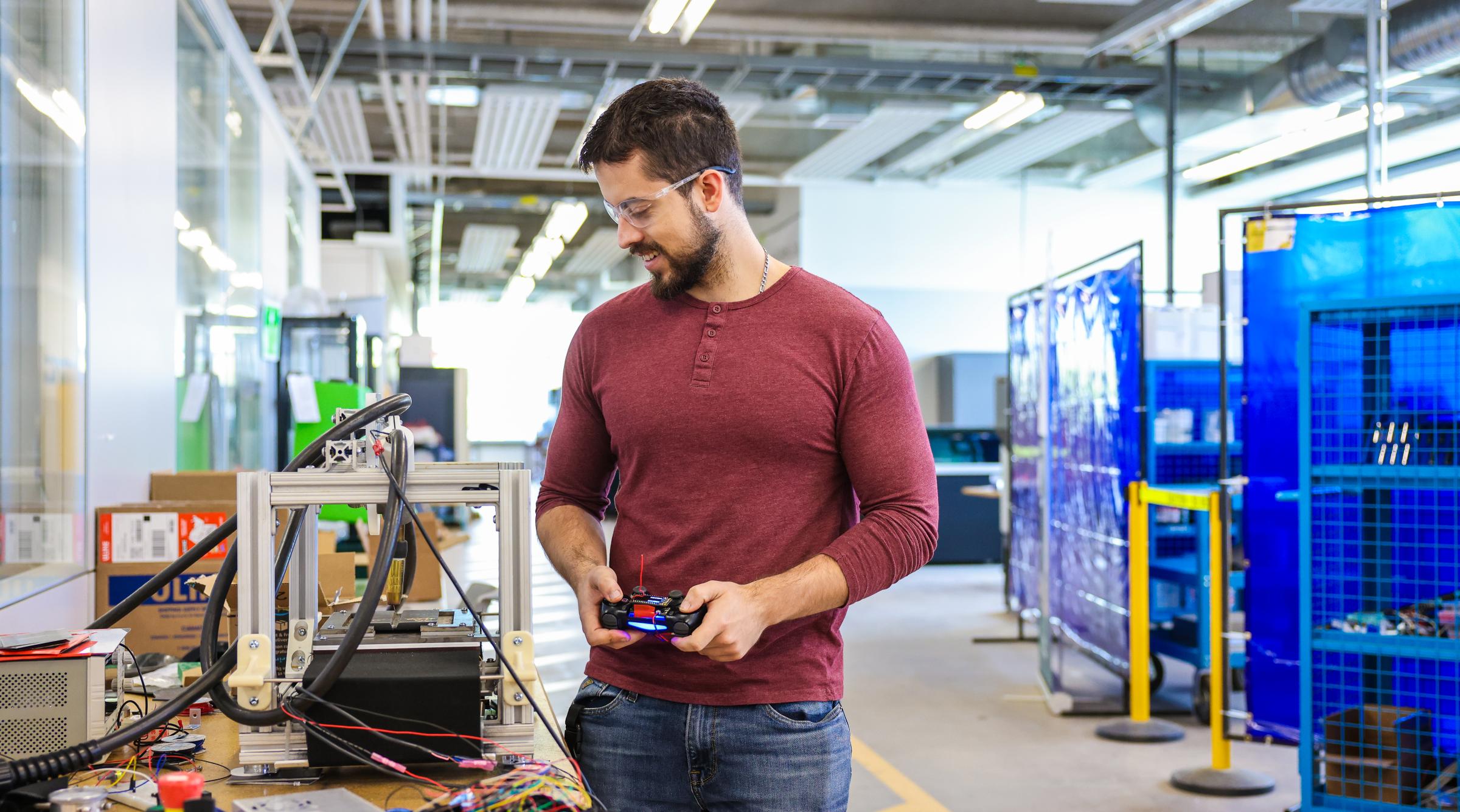 Student stands with a remote control looking at a table full of high-tech equipment