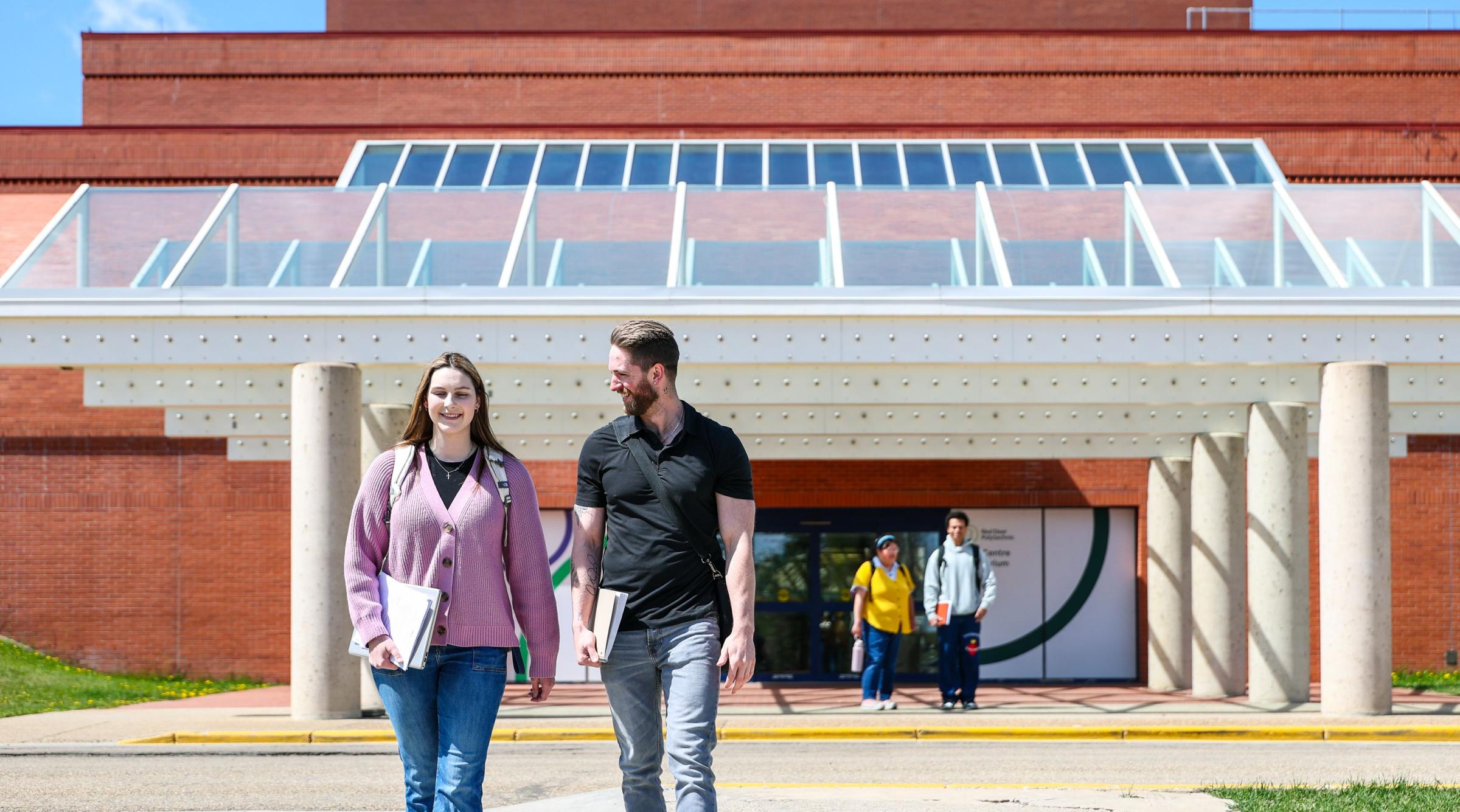 Two students cross the street in front of the Arts Centre. Two more students stand in the background