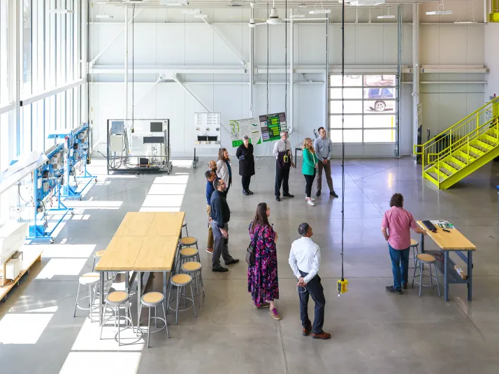 The open area of the AEL with large windows, bay doors, training technology and tables. A small group gathers in the center of the large space.