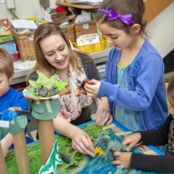 Student helping children with dinosaur model