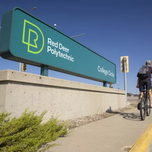 Student riding bike by campus sign