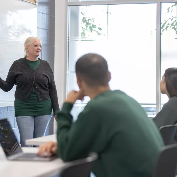 Instructor teaching students from a mounted white board.