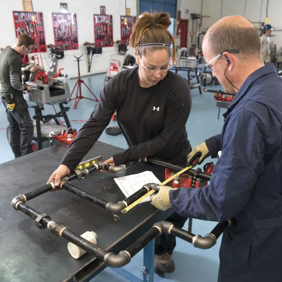 Plumber instructor and student measuring a pipe