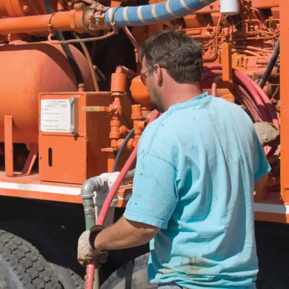 Man with blue shirt examining a orange water truck