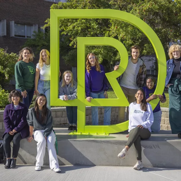 Students sitting by RDP sculpture outside main campus entrance