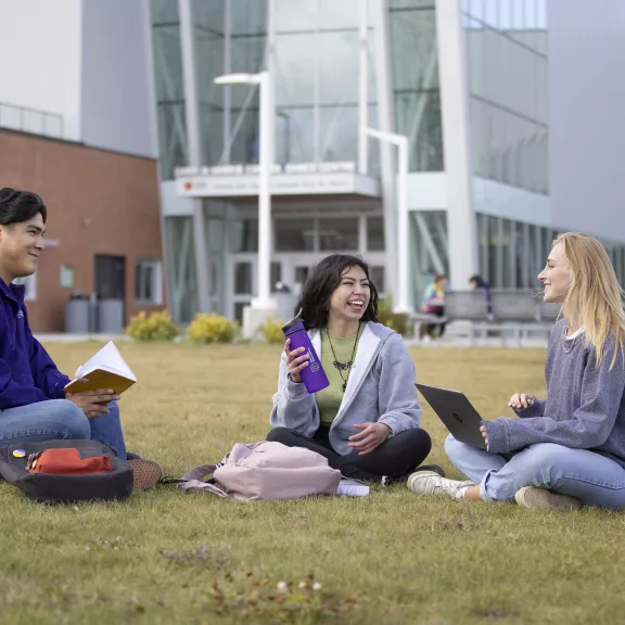 Three students sitting on grass outside Harris Centre