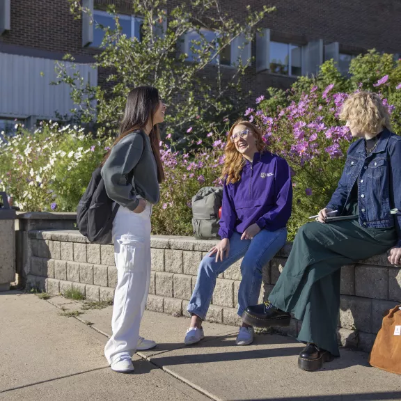 Three students talking outside by the summer flowers