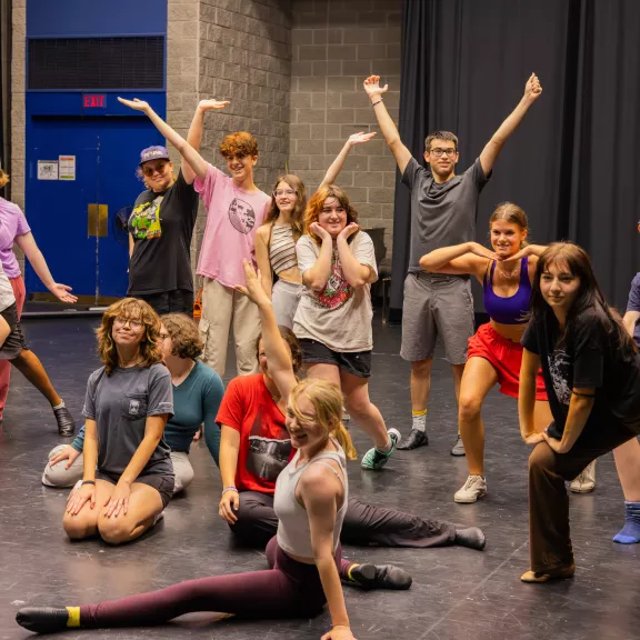 A group of teenagers posing in various dance positions on a stage