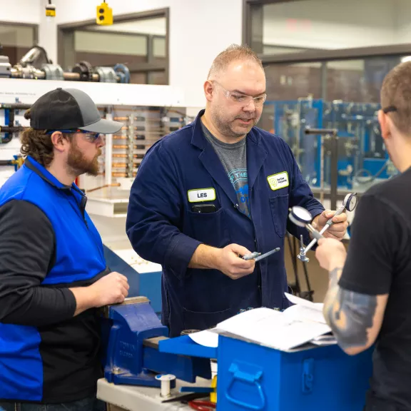 An instructor in blue coveralls introducing students to various tools.