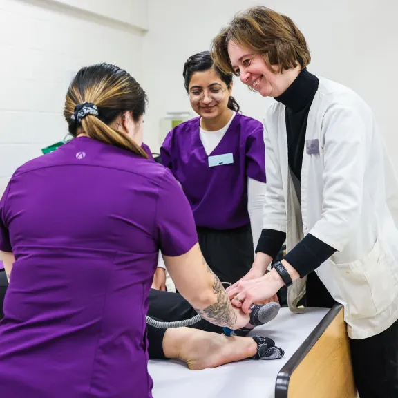 A group of student nurses and a faculty member practice their techniques on another student