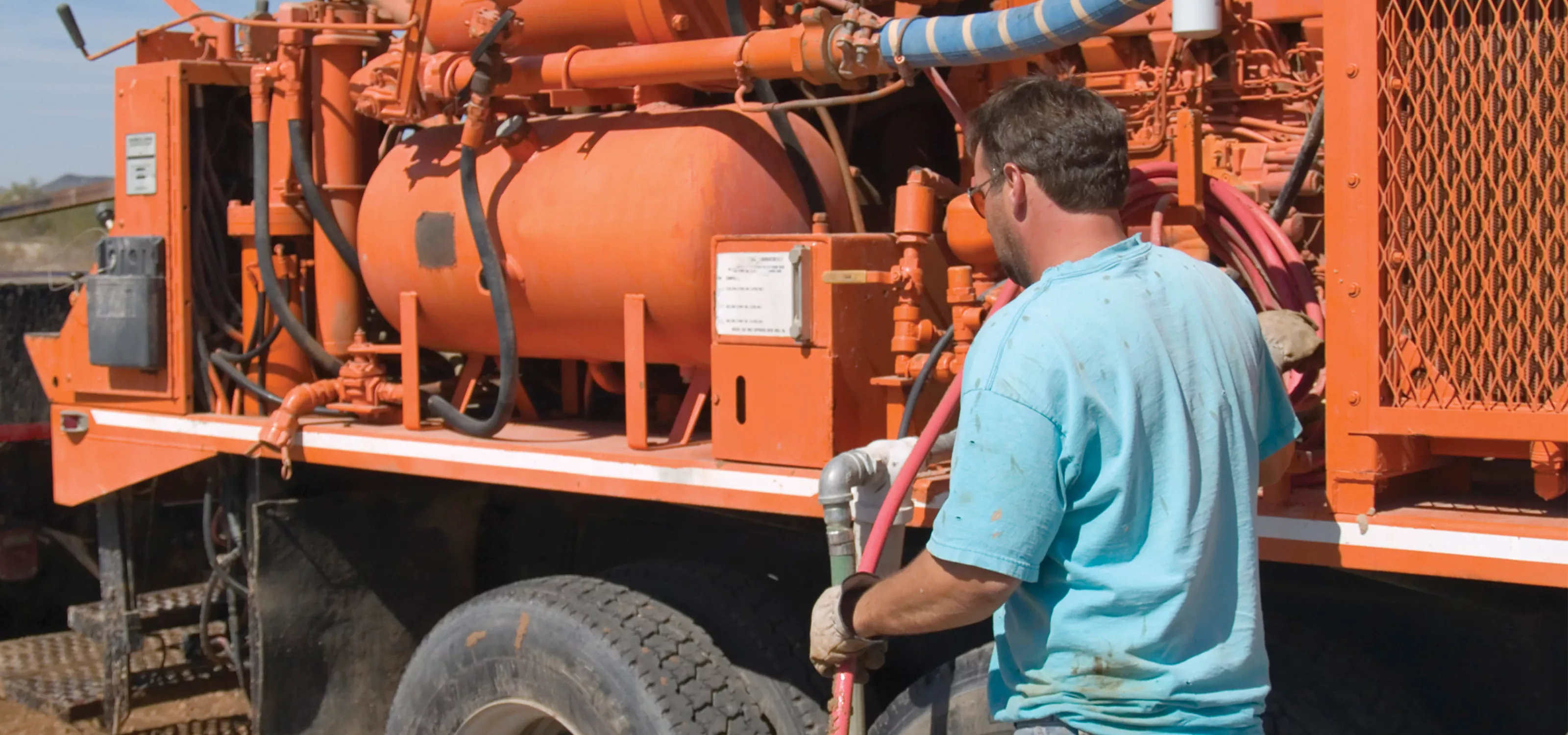 Man with blue shirt examining a orange water truck